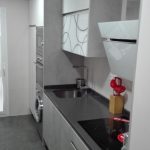 Una combinación de materiales, la zona de arriba blanco brillo y zona de abajo una puerta gris en mate y los decorativos también en gris,con tirador uñero en inox. y encimera de Silestone en color Marengo, vemos la vitrina en cristal blanco con decorado en el mismo color que la encimera.